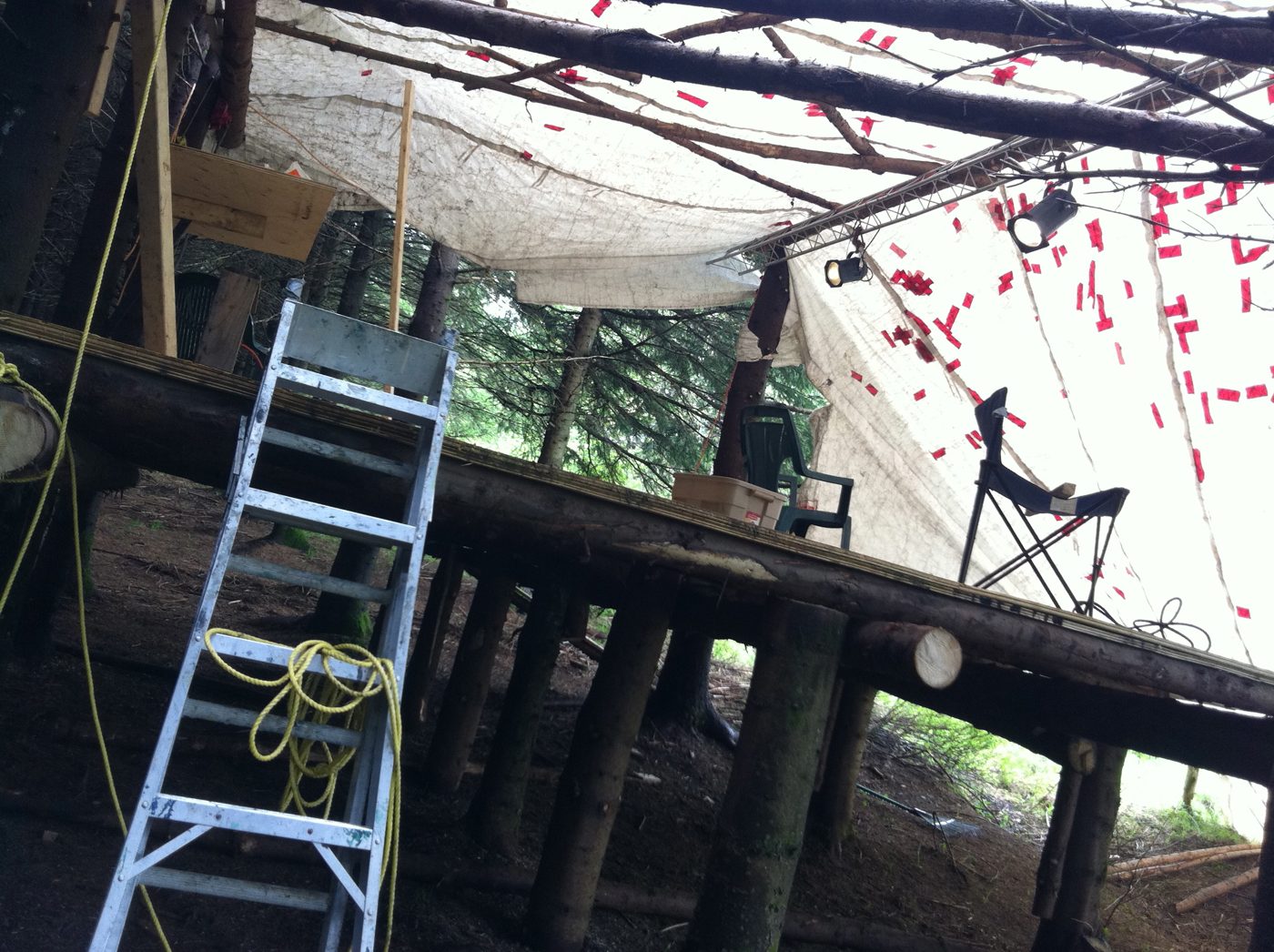 The covered stage under construction: ladder, tarp, string lights.